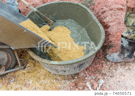 A worker mixes cement with sand directly in a pickup. Preparation of the mixture A worker mixes cement with sand directly in a pickup. Preparation of the mixture 74050571