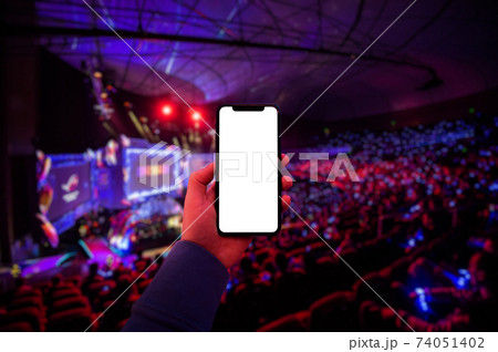 Man's hand using digital application on the mobile smart phone at esport event at big arena. Blank screen with copy space. 74051402