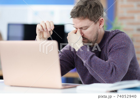 Tired man siting in front of laptop screen and holding glasses in hands 74052940