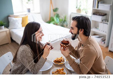 Young couple in love eating hamburgers indoors at home. 74053523