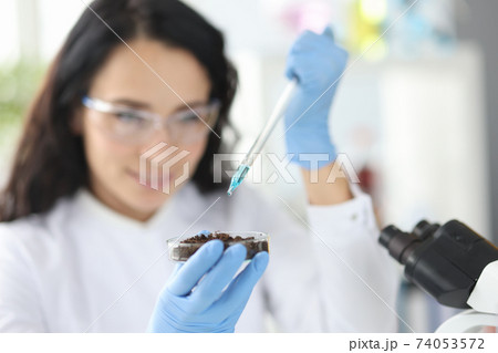 Female scientist dripping liquid from pipette into petri dish with soil Female scientist dripping liquid from pipette into petri dish with soil 74053572