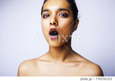 young pretty indian woman with dry fruit in mouth on white background young pretty indian woman with dry fruit in mouth on white background 74058103