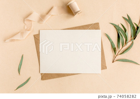 Mockup invitation, blank greeting card and craft envelope, green leaves eucalyptus. Flat lay, top view. 74058282
