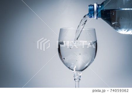 Pouring water into a glass goblet from a plastic bottle. 74059362