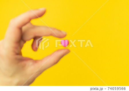 The hand takes a pink heart isolated in the center on an empty colorful yellow background. Symbol of 74059566