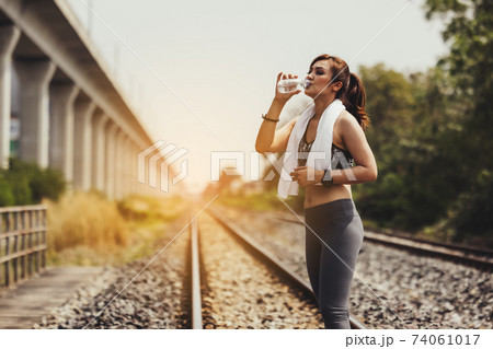 Sportswoman drinking water at old railway track for workout and exercise 74061017