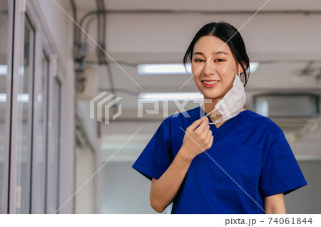 Young beautiful Asian medical nurse in scrub uniform at hospital prepared to wear a face mask. Professional medic at workplace during Covid19 pandemic 74061844