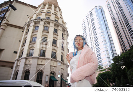 Happy stylish young hipster woman with long blue hair pink jacket, hat on the street in urban city. 74063553