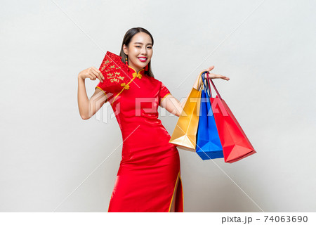 Asian woman in traditional qipao dress holding bags and red envelopes 74063690