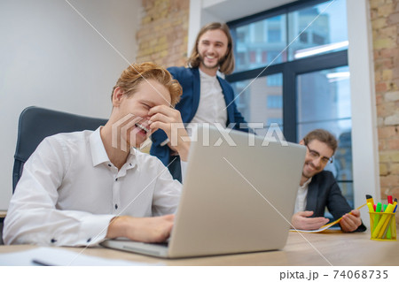 Man behind laptop and colleagues funny laughing Man behind laptop and colleagues funny laughing 74068735