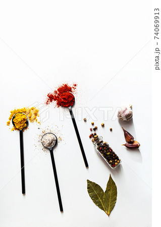 Various spices in black spoons. Salt, curry, turmeric, ground paprika, bay leaf, garlic, peppercorns flat lay on a white background 74069913