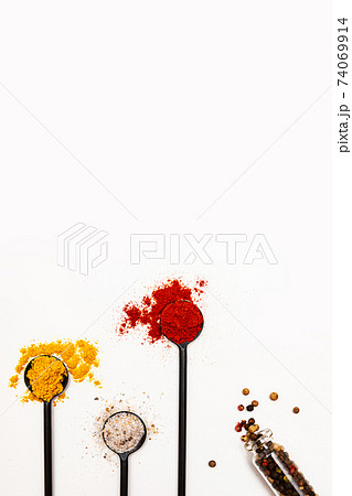 Various spices in black spoons. Salt, curry, turmeric, ground paprika, bay leaf, garlic, peppercorns flat lay on a white background Various spices in black spoons. Salt, curry, turmeric, ground paprika, bay leaf, garlic, peppercorns flat lay on a white background 74069914