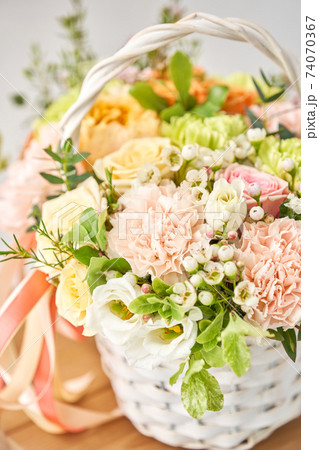 Small flower shop and Flowers delivery. Flower arrangement in Wicker basket. Beautiful bouquet of mixed flowers on wooden table. Handsome fresh bouquet. 74070367