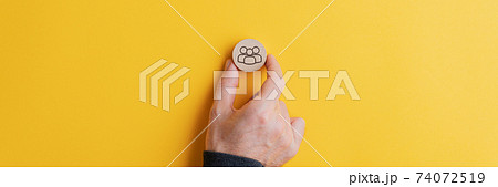 Male hand placing wooden cut circle with people symbol on it on yellow background 74072519