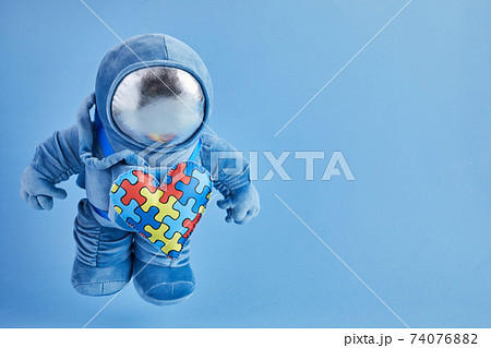 World Autism awareness day background. Blue plush astronaut toy with puzzle heart, autism symbol, on blue background World Autism awareness day background. Blue plush astronaut toy with puzzle heart, autism symbol, on blue background 74076882