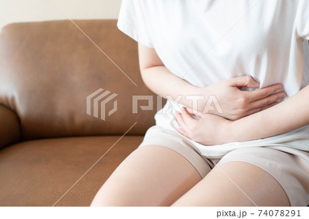 Young female suffering form stomach ache while sitting on couch at home. Causes of abdominal pain include menstruation pain, gastritis, stomach ulcer, food poisoning, diarrhea or IBS. Young female suffering form stomach ache while sitting on couch at home. Causes of abdominal pain include menstruation pain, gastritis, stomach ulcer, food poisoning, diarrhea or IBS. 74078291