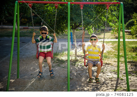 Two little kid boys having fun with swing on outdoor playground. Two little kid boys having fun with swing on outdoor playground. 74081125