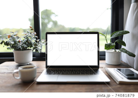 laptop mock up white blank screen with phone and coffee cup and plant pot on wooden table in front of windows  74081879