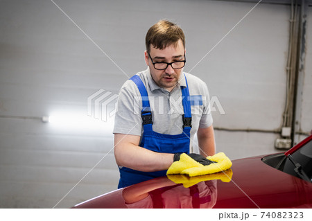Man cleans car surface from drops using wiper. Man cleans car surface from drops using wiper. 74082323