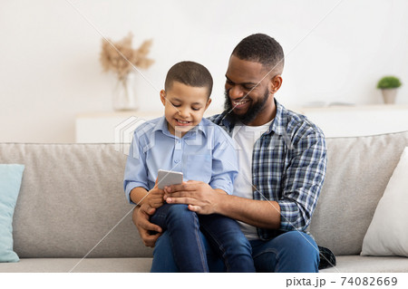 Little African Boy And His Dad Using Smartphone At Home Little African Boy And His Dad Using Smartphone At Home 74082669