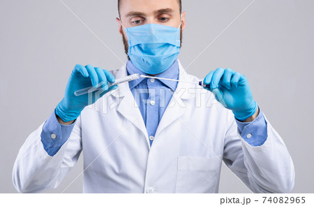 Medical doctor in face mask and gloves holding covid-19 PCR test tube on light grey studio background, panorama 74082965