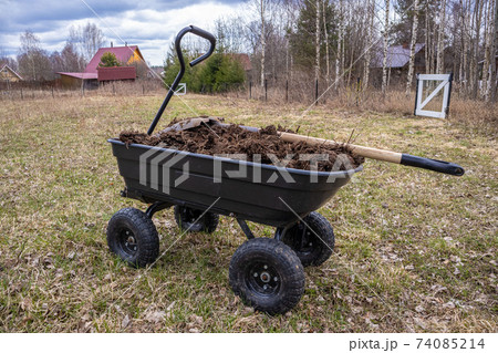 humus in a four-wheeled garden cart. Cloudy spring day humus in a four-wheeled garden cart. Cloudy spring day 74085214