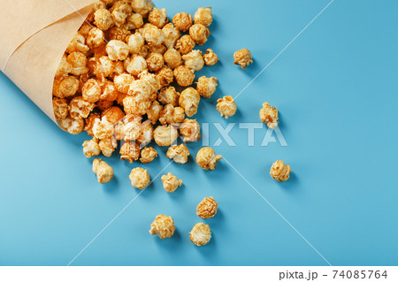 Popcorn in caramel glaze in a paper envelope on a blue background. Popcorn in caramel glaze in a paper envelope on a blue background. 74085764