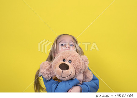 Blond child girl holding toy Teddy bear. Kid girl in modern clothes with long hair play with Teddy bear 74087734