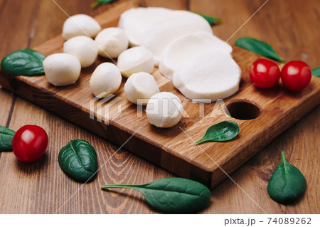 White small mozzarella cheese balls, spinach leaves and tomatoes on wooden board. 74089262