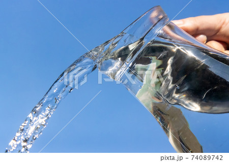 A Clear water flowing from a glass jug on a blue background. 74089742