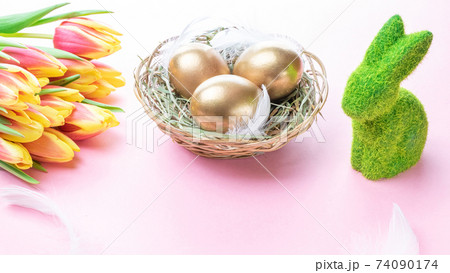 Easter Golden colour eggs in basket with spring tulips, white feathers on pastel pink background in Happy Easter decoration. Festive decoration. Easter Golden colour eggs in basket with spring tulips, white feathers on pastel pink background in Happy Easter decoration. Festive decoration. 74090174