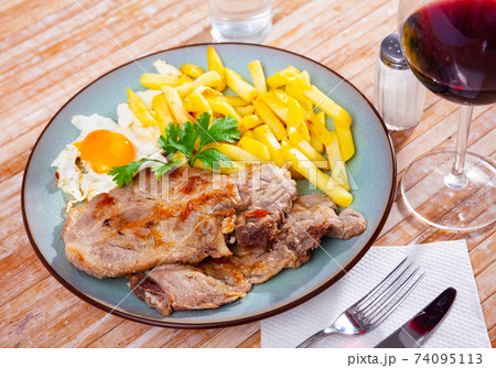 close up of grilled pork with fried potato and egg served on blue plate on wooden table 74095113