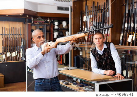 Hispanic man examining break-barrel air rifle in gunsmith store 74096541