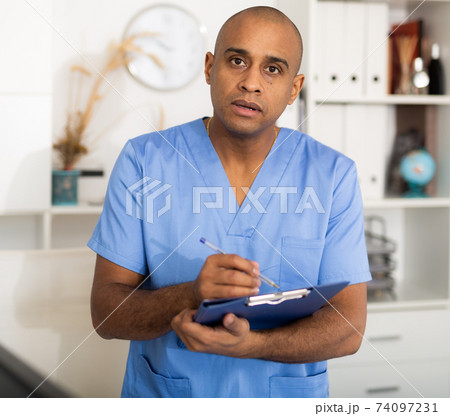 Portrait of friendly male doctor or nurse wearing blue scrubs uniform and stethoscope 74097231