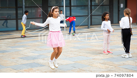 Happy tweenager girl skipping rope in schoolyard Happy tweenager girl skipping rope in schoolyard 74097804