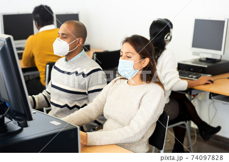 Female student in face mask working on computer in library 74097828
