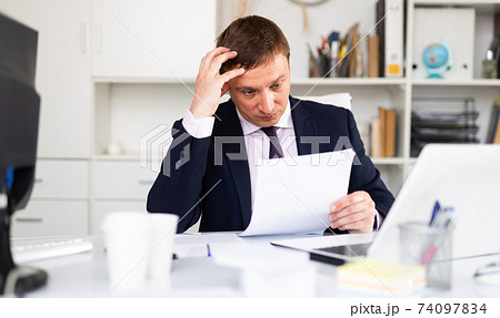 Pensive businessman working with papers Pensive businessman working with papers 74097834