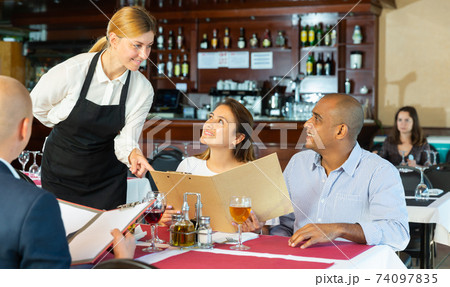 Restaurant guests will choose dish from the menu. Polite waitress helps with choice Restaurant guests will choose dish from the menu. Polite waitress helps with choice 74097835