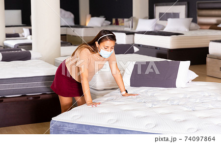 Woman wearing protective mask choosing mattress at store Woman wearing protective mask choosing mattress at store 74097864