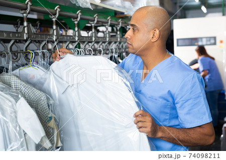 Male worker of laundry inspecting clothing after dry cleaning Male worker of laundry inspecting clothing after dry cleaning 74098211