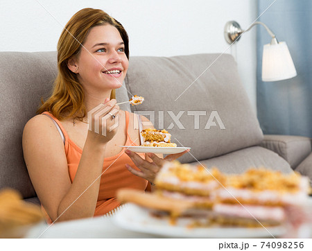 Cheerful female eating sweet cake at home Cheerful female eating sweet cake at home 74098256