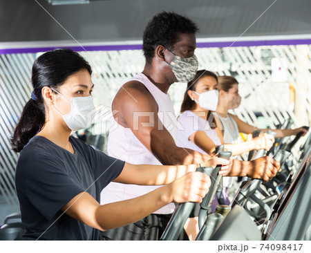 Active people in protective masks having running elliptical trainer class in club Active people in protective masks having running elliptical trainer class in club 74098417