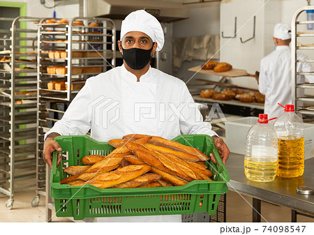 Baker in mask holding crate with bread 74098547