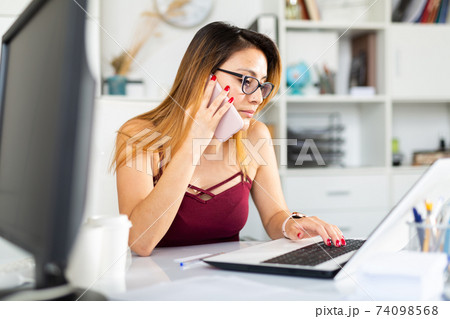 Woman using phone and working with laptop in office Woman using phone and working with laptop in office 74098568