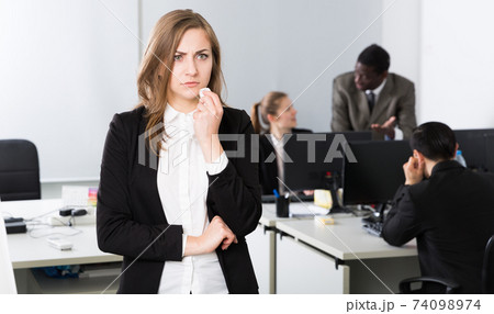 Unhappy businesswoman standing in office, working colleagues Unhappy businesswoman standing in office, working colleagues 74098974