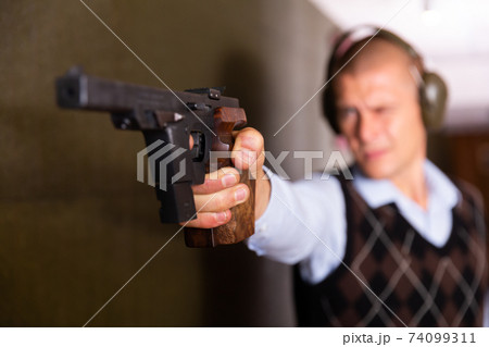 Hand of shooter squeezing pistol grip and pressing trigger at firing range Hand of shooter squeezing pistol grip and pressing trigger at firing range 74099311