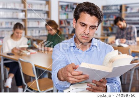Focused man browsing books in library 74099760