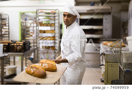 man in chefs uniform with bread on shovel in bakery 74099959