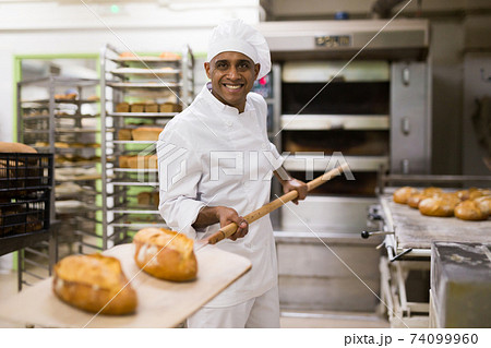 Baker pulls hot bread out of oven Baker pulls hot bread out of oven 74099960