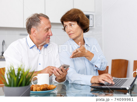 Mature man and woman using smartphone and working at laptop 74099961